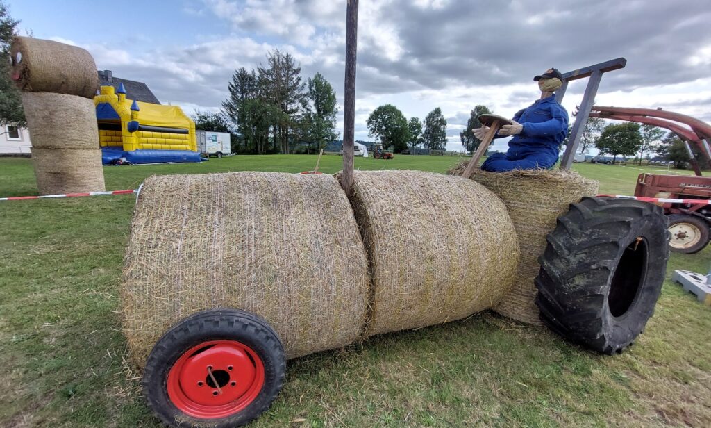Strohtraktor mit Strohfigur auf Dorffest in Wawern (Eifel) – kreative Heuballen-Skulptur mit Traktor-Optik, im Hintergrund Hüpfburg und Festwiese.