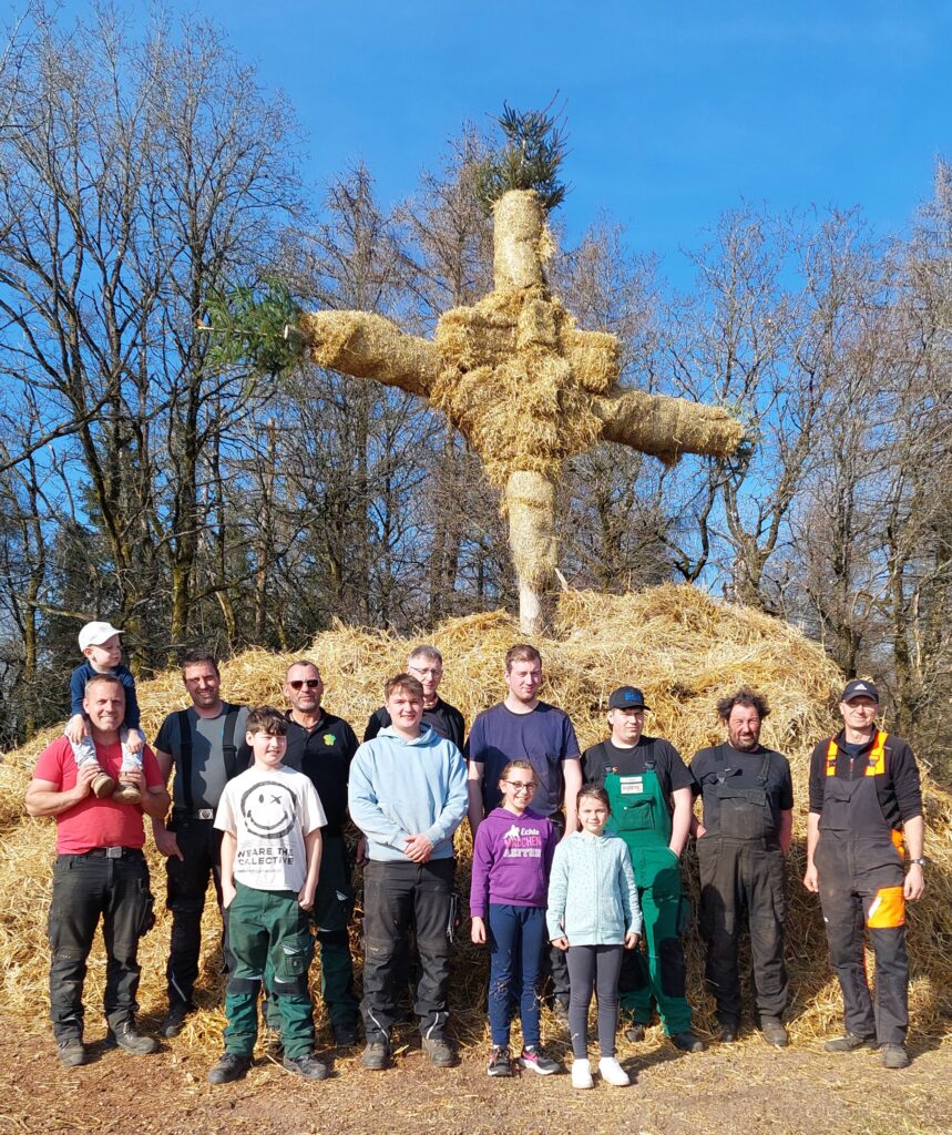 Winterverbrennen in Wawern: Dorfgemeinschaft baut symbolische Strohpuppe zur traditionellen Winterverbrennung – gemeinschaftliche Aktion mit Kindern und Erwachsenen bei sonnigem Wetter