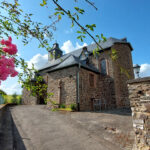 Historische Kapelle in Wawern bei Sonnenschein mit Natursteinmauerwerk und blühenden Rosen im Vordergrund – idyllisches Kulturerbe im Eifelkreis Bitburg-Prüm.