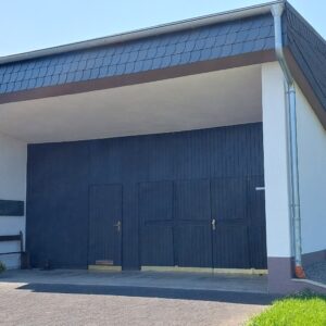 Friedhofskapelle in Wawern bei Sonnenschein – moderner Bau mit dunkler Holztür, Gedenktafeln, Blumenbank und gepflegtem Außengelände im Grünen